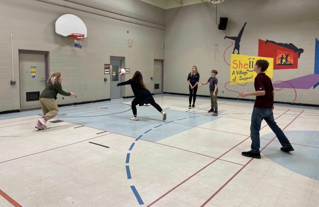 One of the youth participants of the Shelldale Family Gateway hits a volleyball in the Shelldale gymnasium. Four of her teammates stand nearby.