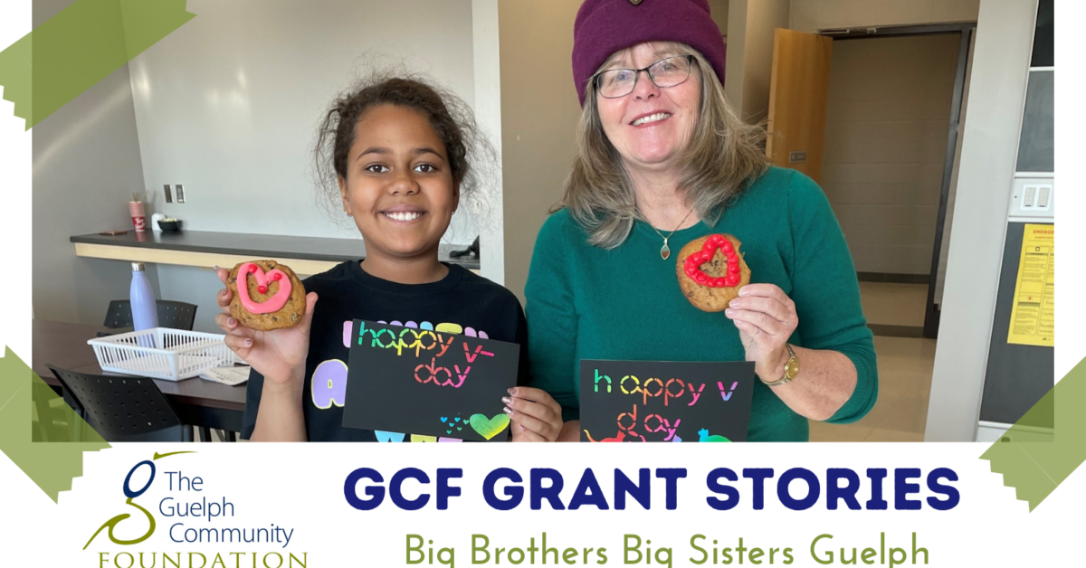GCF Grant Stories Big Brothers Big Sisters Guelph: A young girl and an older woman standing and smiling together holding heart decorated cookies in a classroom
