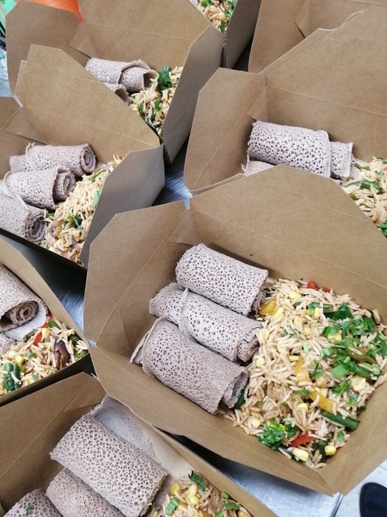 Many brown food boxes opened to reveal three porous wraps with long grain rice and greenery