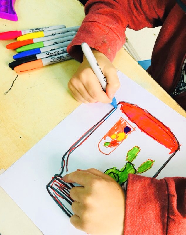 A small hand painting a jar over a table using sharpie colors.