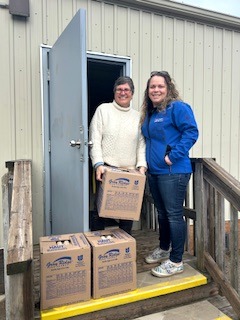 Two women smiling and standing holding and delivering boxes labeled "Unilever". 