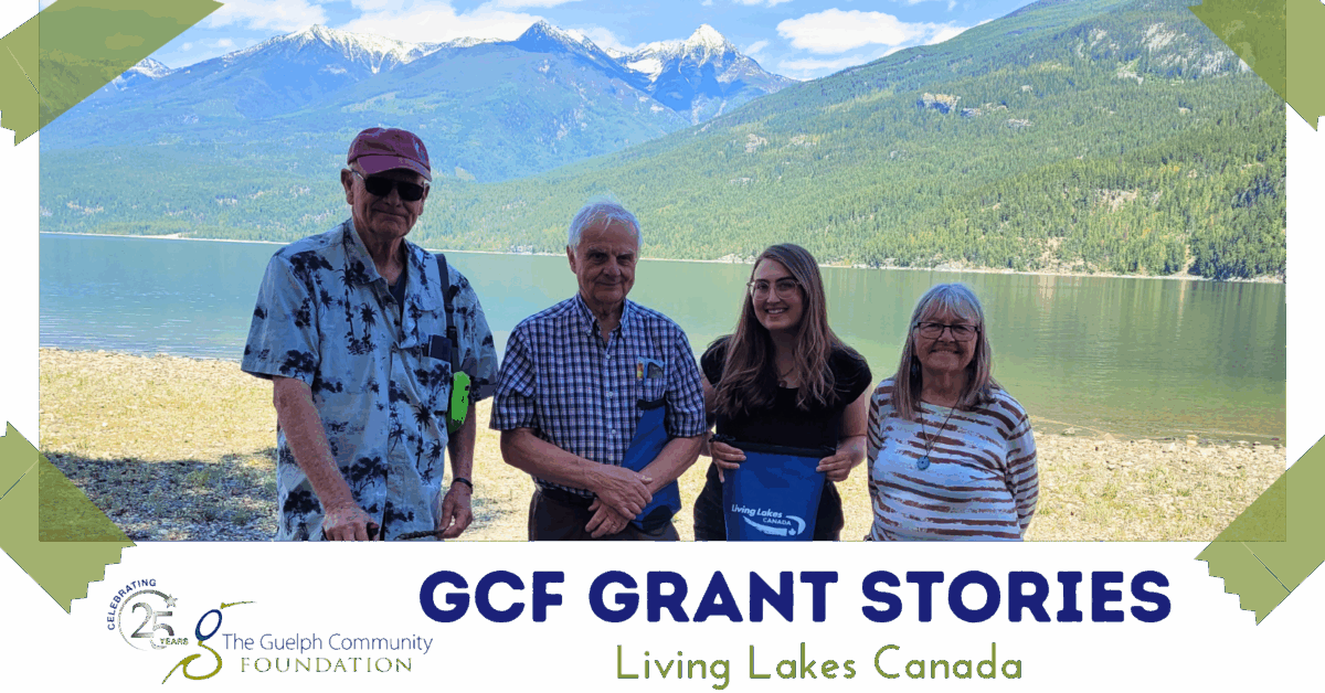 Outdoor photo of four people by a clear lake with expansive mountain range and blue sky behind them.