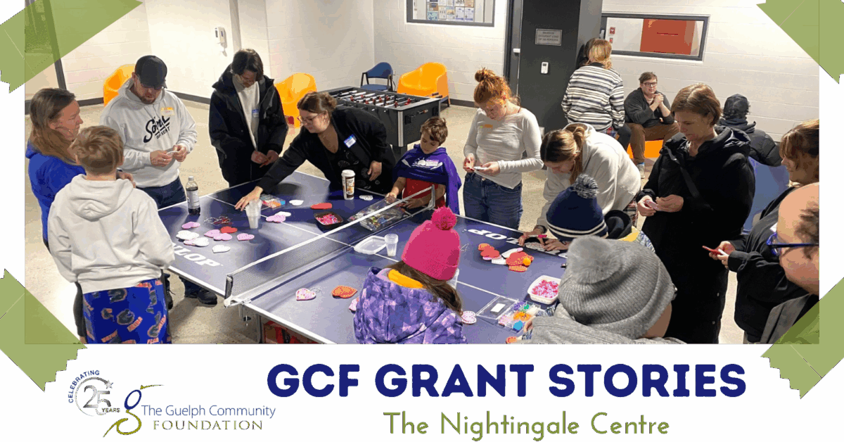 Group of people gathered around a ping pong table crafting heart-shaped decorations indoors.
