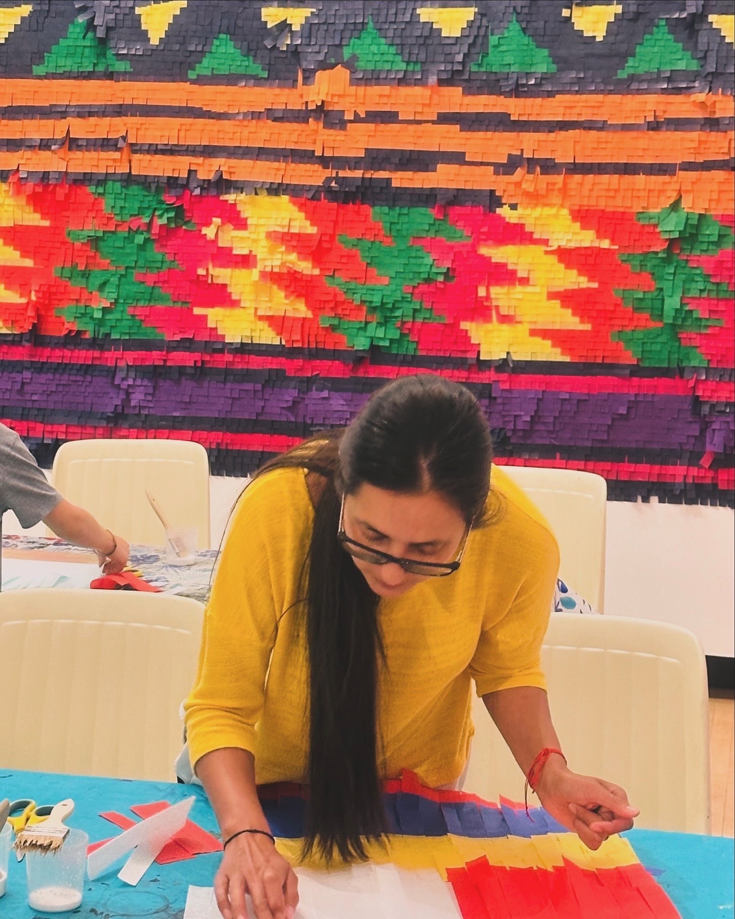 Woman collaborates on a colorful craft project using red and yellow fabric at a community art event.