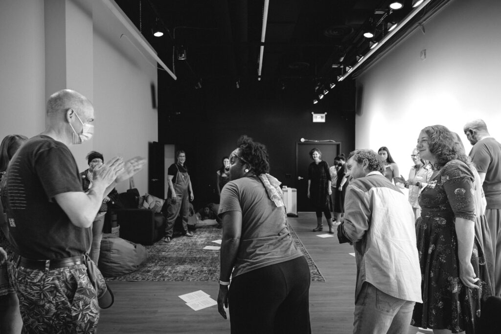 Group of people standing in a spacious room engaged in an interactive workshop or rehearsal activity.