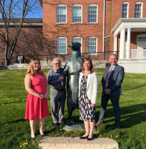 staff photo, four people in formal attire standing with the AGG Bear statue