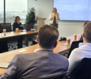 Photo of out of focus female speaker presenting in front of guests at tables in focus