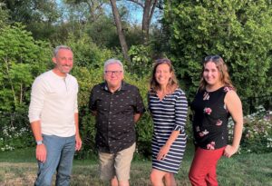 staff photo of four summery people smiling with trees behind them