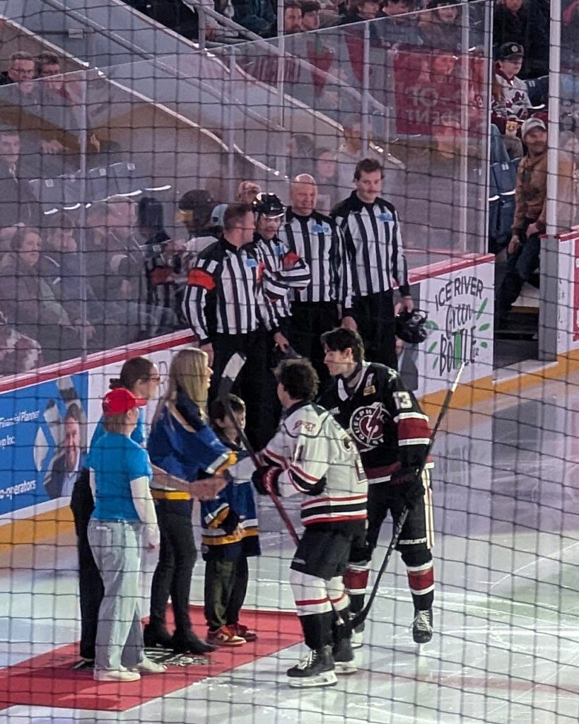 Guelph Storm Hockey players and officials gathered with event reps on the ice in a packed hockey arena.