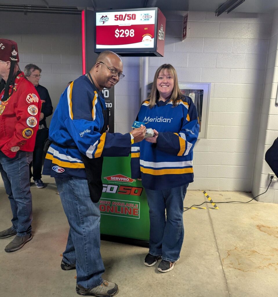 Two Meridian CU employees in the hockey arena showing how to buy 50/50 tickets.