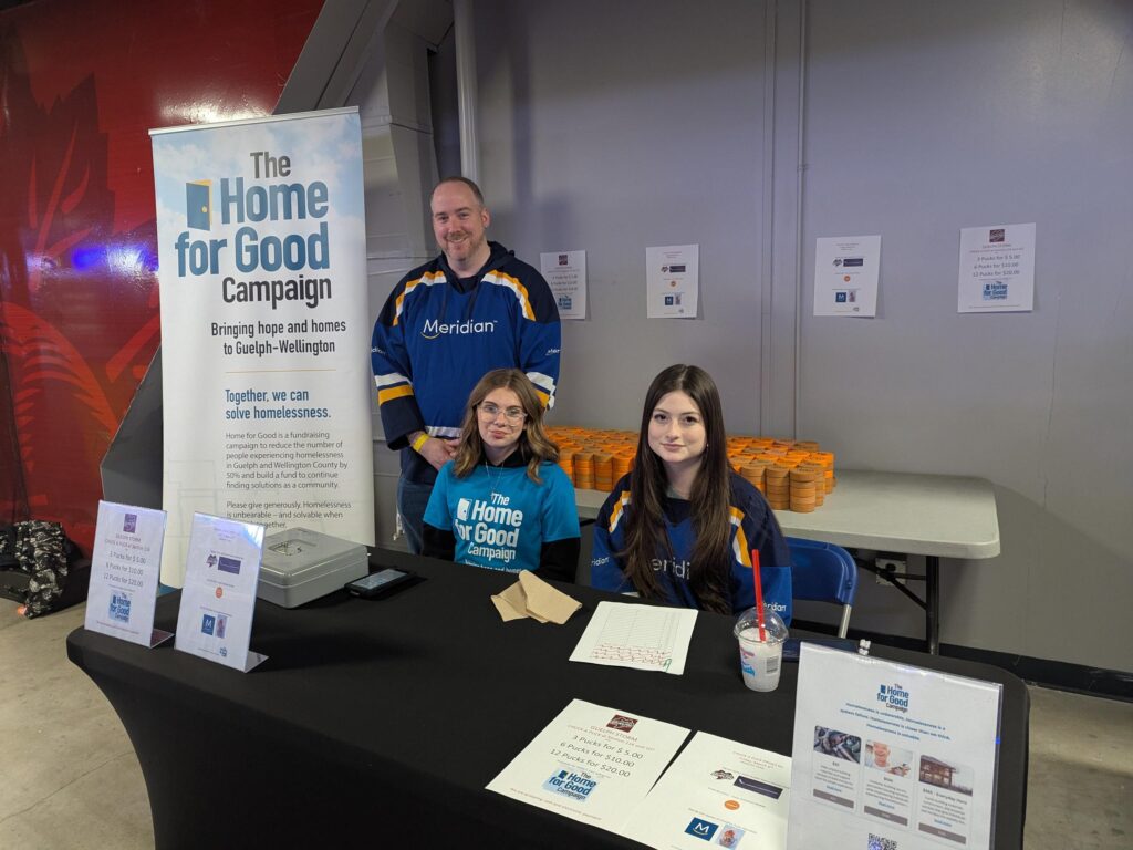 Three volunteers at the Home for Good Campaign table selling Chuck-a-pucks with orange pucks behind them.