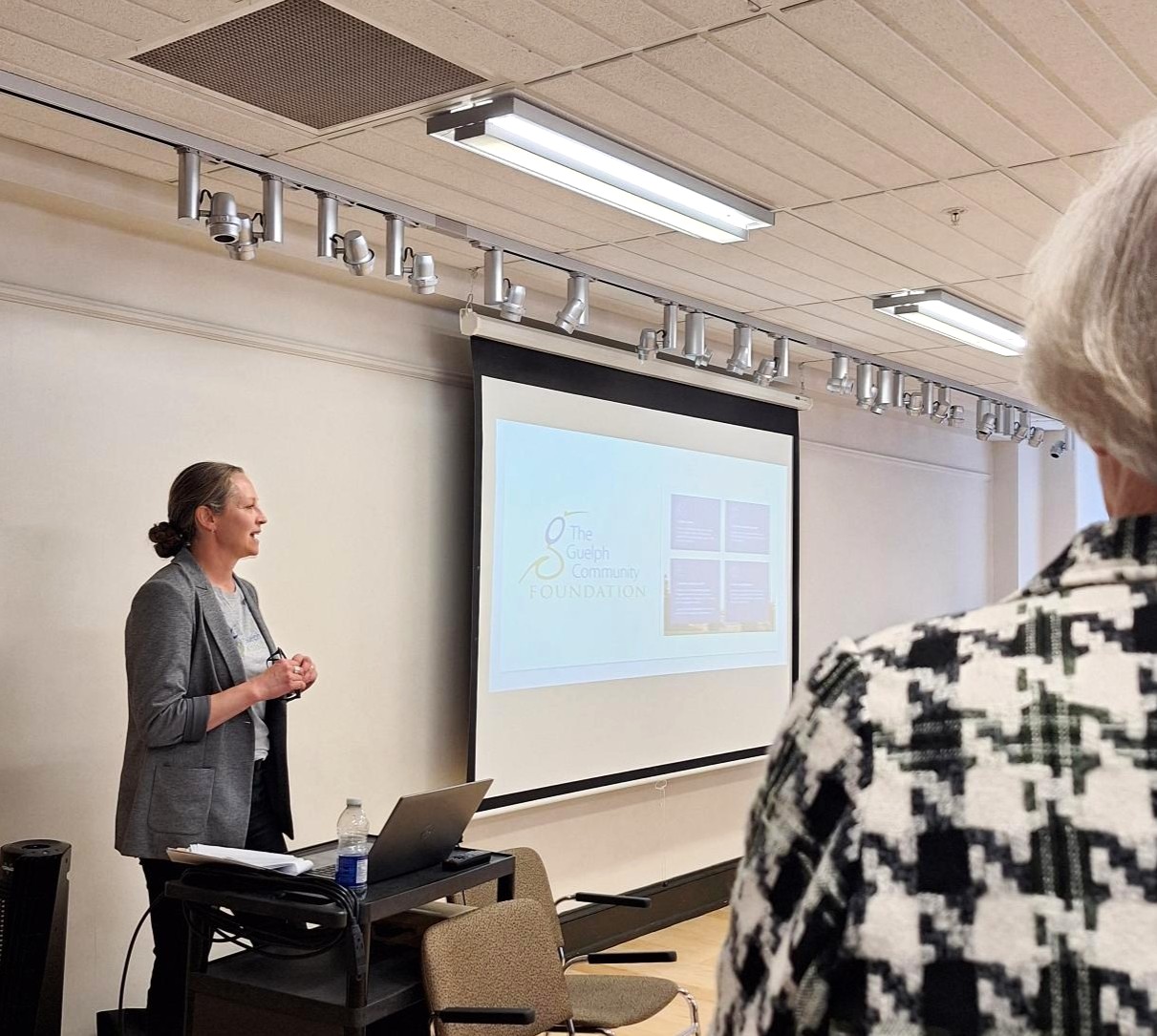 Woman in a gray blazer giving a presentation with a projection screen