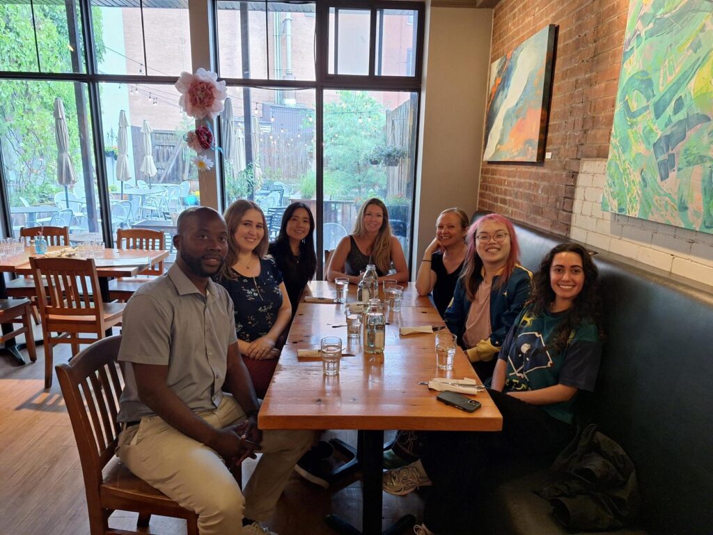 The GCF staff at lunch; seven people smiling and sitting around a wooden table in a cozy restaurant with brick walls and large windows.