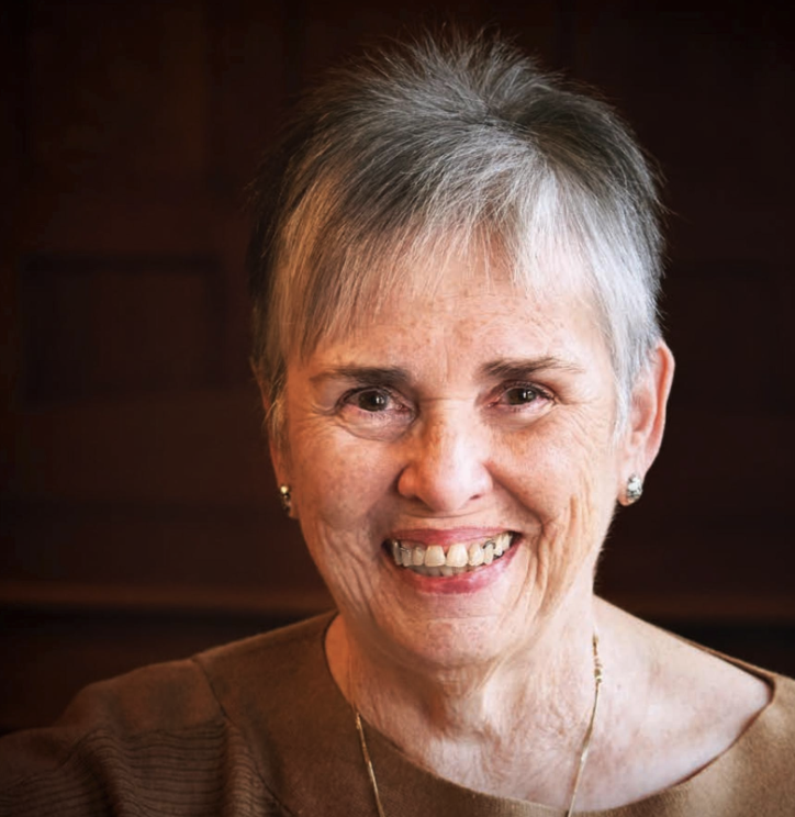 Smiling elderly woman with short gray hair and earrings against a dark background.