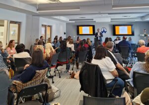 A facilitator leads an interactive group activity at the front of the room while participants respond and engage from their seats during a symposium.