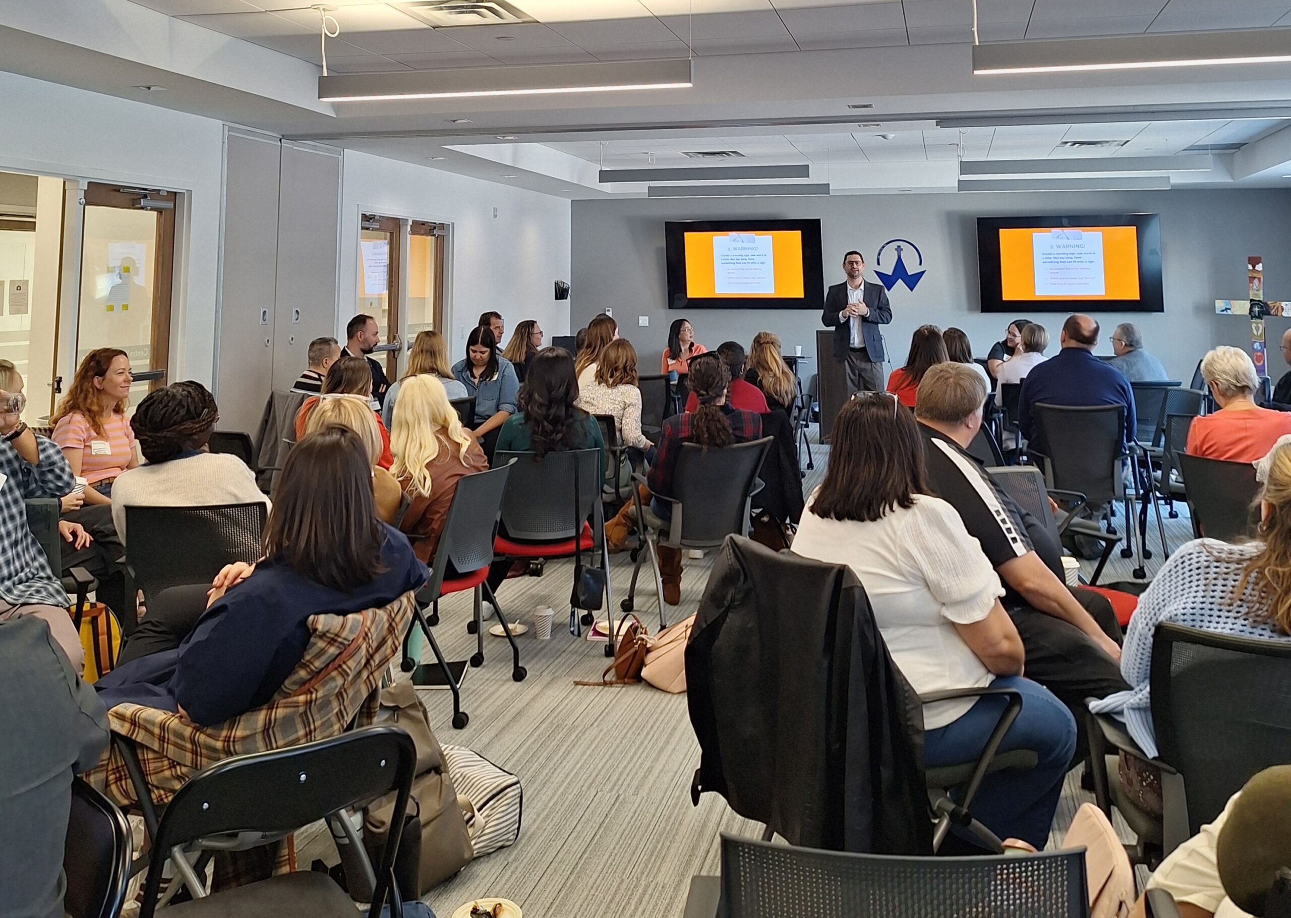 A facilitator leads an interactive group activity at the front of the room while participants respond and engage from their seats during a symposium.
