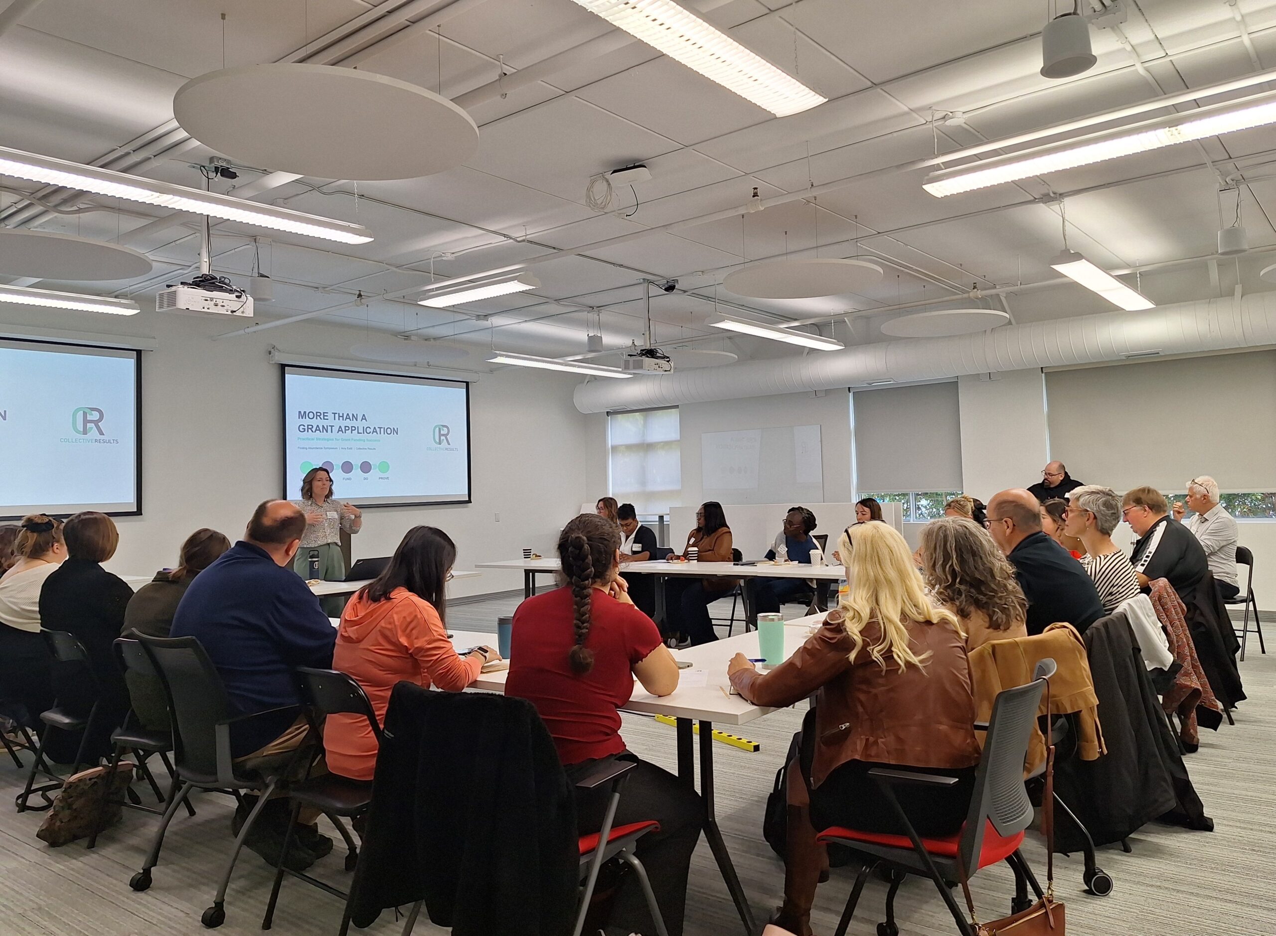 A presenter leads a workshop session while attendees seated around tables listen and participate in discussion during the Finding Abundance symposium.