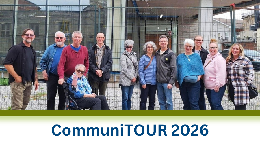 Group of twelve adults posing outdoors in front of a metal fence and building, dressed casually for cool weather. Text below reads CommuniTOUR 2026.