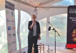 A female speaker stands inside a tent with a microphone